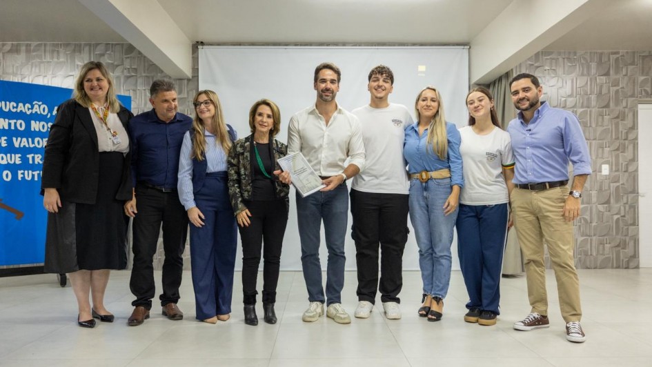 Registro coletivo em ambiente interno, com um grupo alinhado lado a lado para foto institucional. O governador ao centro segura um documento, indicando ato formal de entrega.
