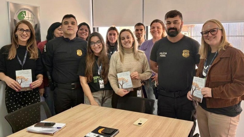 Foto mostra equipe da Pol&iacute;cia Penal e da UCPel runidos e exibindo um documento, dentro de uma sala.