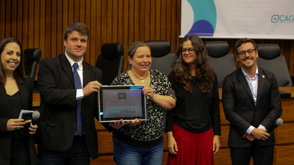 A imagem mostra um grupo de cinco pessoas alinhadas segurando um pr&ecirc;mio. 