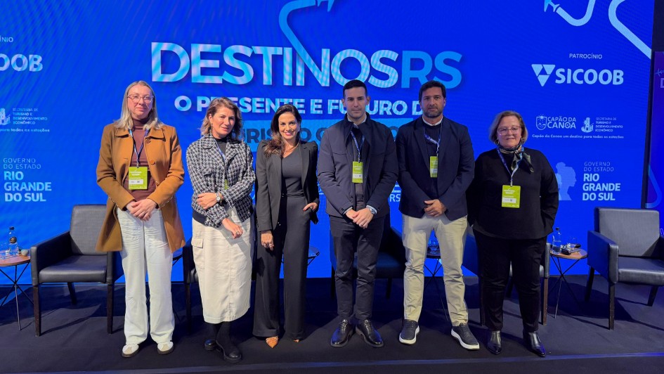 Registro coletivo sobre palco de evento institucional, com grupo alinhado diante de painel azul com o texto &ldquo;DESTINOS RS &ndash; O presente e futuro&rdquo;, logotipos de patrocinadores e identidade do Governo do Estado.