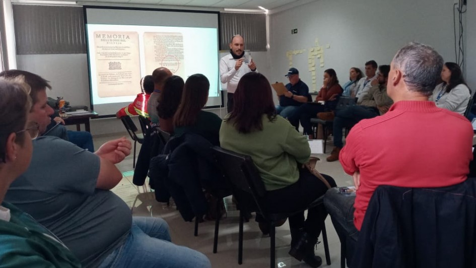 Foto mostra palestrante falando diante dos participantes da oficina em uma sala de aula.