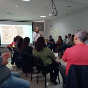 Foto mostra palestrante falando diante dos participantes da oficina em uma sala de aula.