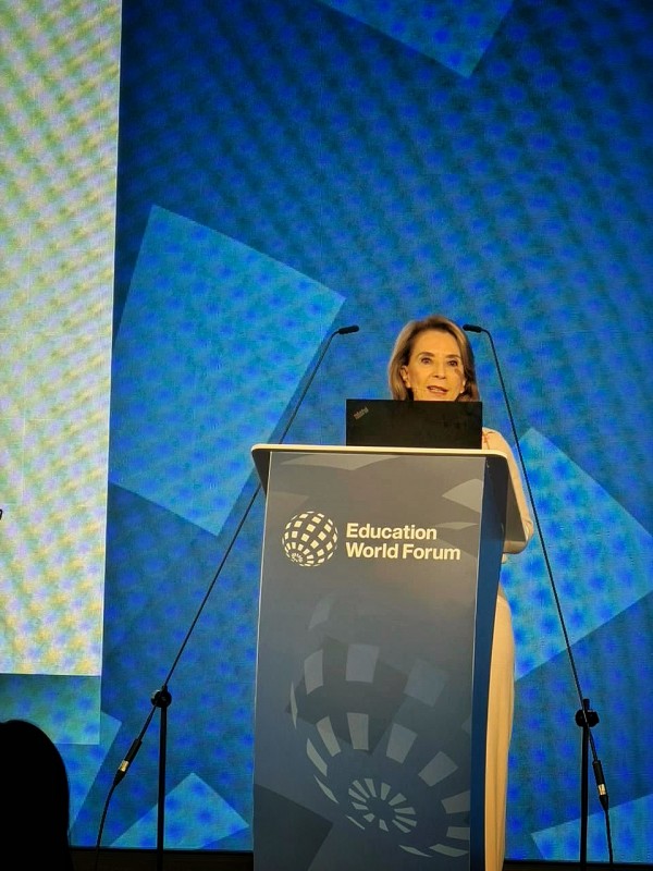 Close de apresentação no Education World Forum, com a secretária da Educação posicionada atrás de púlpito identificado com o logotipo do evento.