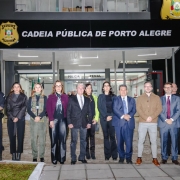 Foto mostra comitiva com o ministro e o secret&aacute;rio na frente da unidade prisional. Ao fundo est&aacute; escrito "Cadeia P&uacute;blica de Porto Alegre" e o bras&atilde;o da Pol&iacute;cia Penal.