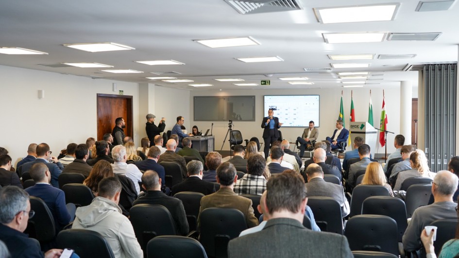 A imagem mostra um audit&oacute;rio lotado e a secret&aacute;ria do Meio Ambiente e Infraestrutura posicionada em p&eacute; no palco, falando ao microfone. 