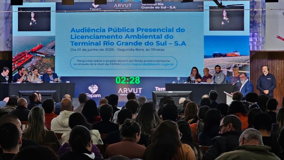 Foto mostra a mesa do evento com plateia assistindo.