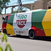 Foto mostra a Unidade M&oacute;vel Tudo F&aacute;cil, um &ocirc;nibus colorido nas cores amarelo, verde e vermelho, com a marca do programa num fundo branco.