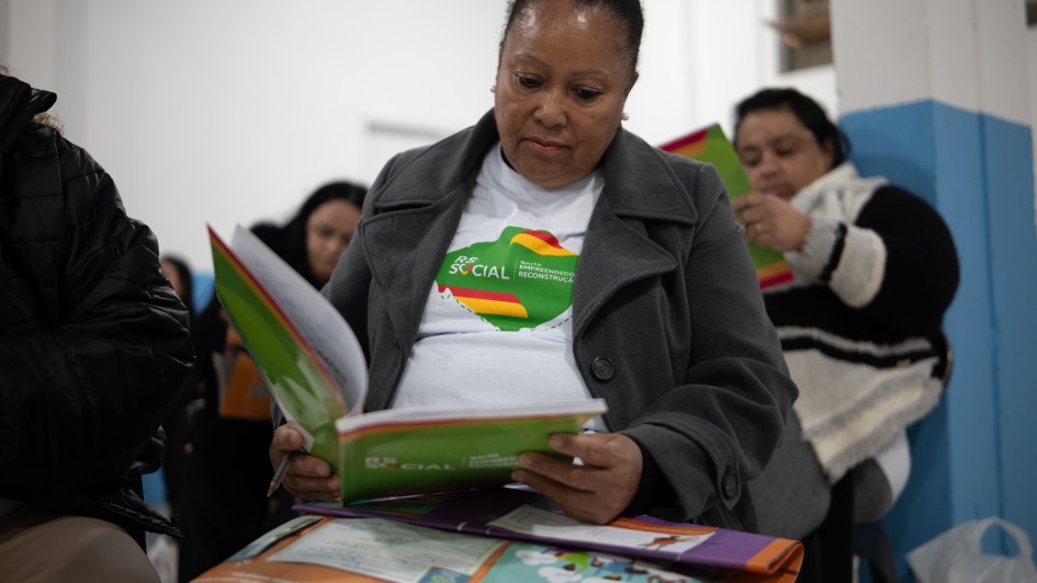 Foto mostra uma participante do programa sentada na sala de aula, lendo um livro com a marca do programa.