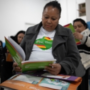 Foto mostra uma participante do programa sentada na sala de aula, lendo um livro com a marca do programa.