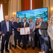 Foto mostra o governador Eduardo Leite  no sal&atilde;o do Pal&aacute;cio Piratini segurando uma pasta com um documento assinado com as autoriza&ccedil;&otilde;es para as obras. Ele est&aacute; acompanhado de outras autoridades, que aplaudem. 