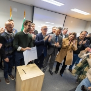 Foto mostra o governador Eduardo Leite segurando um documento assinado. Prefeitos e outras autoridades aplaudem o ato.