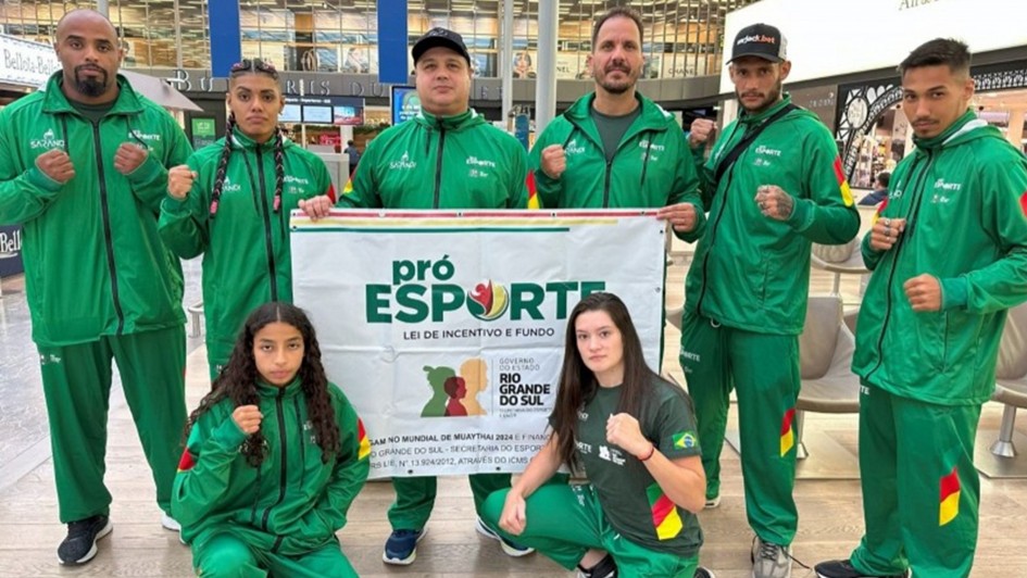 Foto mostra delega&ccedil;&atilde;o posando perfilados com a bandeira do Pr&oacute;-Esporte RS. O uniforme deles &eacute; verde com detalhes da bandeira do Rio Grande do Sul.