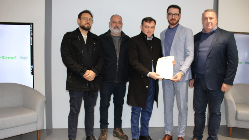 Foto mostra secret&aacute;rio e representantes da Microempa durante assinatura documento.