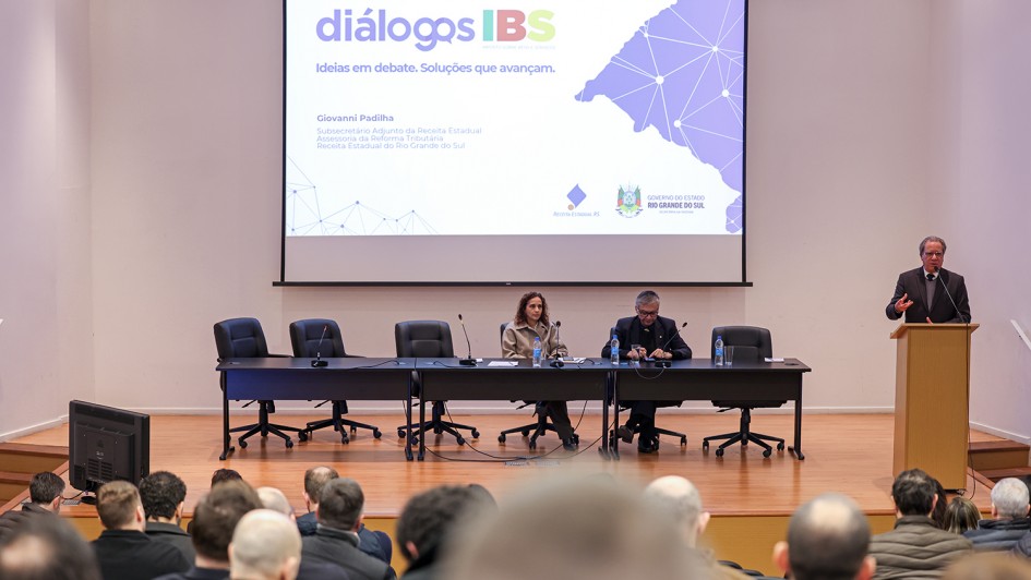Foto mostra palestrante no p&uacute;lpito, no palco do evento, falando para a plateia.