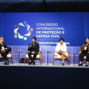 A imagem mostra um palco com quatro palestrantes sentados. Ao fundo, em um painel, l&ecirc;-se "Congresso Internacional de Prote&ccedil;&atilde;o e Defesa Civil". 