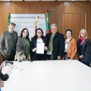 Um grupo de pessoas se posiciona em p&eacute; atr&aacute;s da mesa para uma foto, enquanto a titular da Sema segura um documento voltado para a c&acirc;mera.