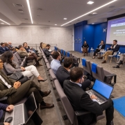 Descri&ccedil;&atilde;o da imagem "Road show na B3 abriu fase de apresenta&ccedil;&atilde;o ao mercado para estudo do projeto que viabiliza institui&ccedil;&atilde;o com 350 leitos 100% SUS.jpeg":

Uma fotografia colorida em plano geral e &acirc;ngulo levemente picado mostra o interior de um audit&oacute;rio moderno durante uma apresenta&ccedil;&atilde;o institucional. A plateia est&aacute; sentada em poltronas dispostas em fileiras inclinadas &agrave; esquerda, enquanto os palestrantes ocupam uma &aacute;rea de palco &agrave; direita.

O Palco e os Palestrantes (&agrave; direita):
&Agrave; frente de uma parede azul-escura com o logotipo branco da "[B]&sup3;" (Bolsa de Valores do Brasil), quatro pessoas est&atilde;o sentadas em cadeiras brancas de estilo moderno com pernas de madeira clara, dispostas em um semic&iacute;rculo:

Da esquerda para a direita: Uma mulher com blusa escura e saia marrom; uma mulher de terno escuro e camisa social clara; o governador Eduardo Leite, vestindo um palet&oacute; escuro sobre camisa branca, cal&ccedil;a bege e sapatos marrons, segurando um microfone e gesticulando enquanto fala; e um homem calvo vestindo um terno cinza ou bege-claro, olhando em dire&ccedil;&atilde;o ao governador.

Atr&aacute;s deles, uma grande tela de proje&ccedil;&atilde;o exibe um slide com o t&iacute;tulo principal: "NOVO HOSPITAL ESTADUAL EM VIAM&Atilde;O - APRESENTA&Ccedil;&Atilde;O DO PROJETO". O slide possui logotipos institucionais no topo, incluindo o do BID (Banco Interamericano de Desenvolvimento) e o do Governo do Estado do Rio Grande do Sul.

A Plateia (&agrave; esquerda e ao centro):
V&aacute;rias pessoas em trajes formais e casuais de neg&oacute;cios assistem &agrave; apresenta&ccedil;&atilde;o.

Em primeiro plano, no canto inferior esquerdo, uma mulher usa &oacute;culos e digita em um notebook prata. Ao lado dela, um homem de &oacute;culos e palet&oacute; verde-oliva acompanha a fala. Atr&aacute;s deles, uma mulher com blusa estampada em preto e branco e cal&ccedil;a branca apoia uma bolsa preta no colo.

Nas fileiras centrais, um homem de terno escuro, sentado de costas para a c&acirc;mera, trabalha em um notebook com a tela azul ligada.

As poltronas do audit&oacute;rio s&atilde;o estofadas em tom cinza-escuro. Algumas poltronas vazias nas fileiras centrais possuem capas azuis nos encostos. No canto superior esquerdo, h&aacute; uma segunda tela menor fixada na parede exibindo o mesmo slide da apresenta&ccedil;&atilde;o.

O Ambiente:
O audit&oacute;rio possui piso acarpetado cinza. No canto inferior direito, h&aacute; um tapete azul retangular com o s&iacute;mbolo internacional de acessibilidade para cadeirantes em branco. O teto &eacute; composto por pain&eacute;is texturizados claros com linhas embutidas de ilumina&ccedil;&atilde;o LED e lumin&aacute;rias spot acesas, criando uma atmosfera clara e profissional.