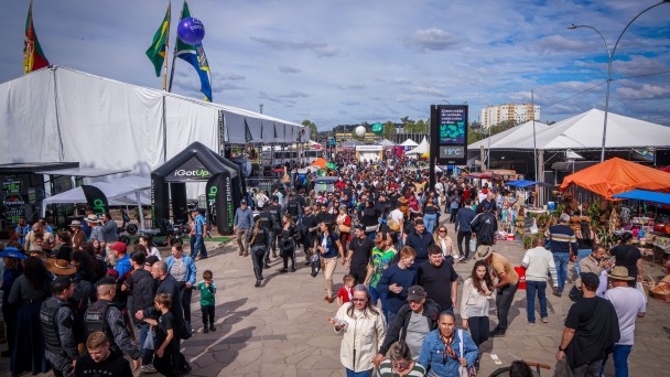 Imagem mostra grande p&uacute;blico na principal entrada da Expointer, com v&aacute;rios toldos de tendas nas laterais.