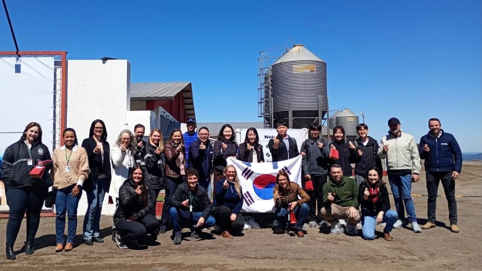 Foto mostra um grupo posando para a foto. No centro, jovens seguram a bandeira da Coreia do Sul. Ao fundo, um silo de propriedade. O c&eacute;u est&aacute; azul, sem nuvens.
