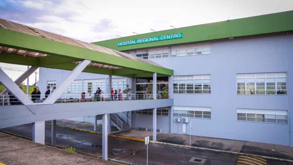 Foto mostra a fachada do Hospital Regional de Santa Maria. Na frente da institui&ccedil;&atilde;o h&aacute; uma passarela com telhado verde. A mesma cor est&aacute; na faixa no alto do pr&eacute;dio. 