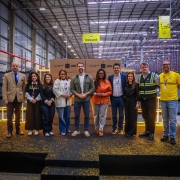 Uma fotografia colorida em plano geral e perspetiva ao n&iacute;vel dos olhos capta a inaugura&ccedil;&atilde;o do centro de distribui&ccedil;&atilde;o do Mercado Livre em Gua&iacute;ba, com a presen&ccedil;a do governador Eduardo Leite, executivos e autoridades.

**As Autoridades e Executivos (ao centro e em primeiro plano):**

* No centro de um palco elevado coberto de alcatifa escura com confetis dourados espalhados pelo ch&atilde;o, dez pessoas posam alinhadas lado a lado para a fotografia oficial.


* Ao centro, o governador Eduardo Leite sorri com as m&atilde;os entrela&ccedil;adas &agrave; frente, vestindo sobrecamisa verde-oliveira sobre t-shirt branca, cal&ccedil;as de ganga escuras e sapatilhas claras.


* &Agrave; sua esquerda (&agrave; direita do observador), encontra-se uma mulher de casaco/blusa de tom laranja-terracota e cal&ccedil;as cinzentas, seguida por executivos de blazer e trajes formais.


* Na extremidade direita, um integrante da equipa veste a t-shirt amarela oficial do Mercado Livre com fita refletora e crach&aacute;, ao lado de um gestor com colete de seguran&ccedil;a refletor de alta visibilidade.


* &Agrave; direita de Eduardo Leite (&agrave; esquerda do observador), alinham-se quatro mulheres em trajes esporte fino e blazer (incluindo uma com t-shirt preta onde se l&ecirc; **"Oi, cheguei! :-)"**) e um homem no extremo esquerdo de blazer bege e gravata.



**O Cen&aacute;rio do Centro de Distribui&ccedil;&atilde;o (ao fundo):**

* Diretamente atr&aacute;s do grupo, ergue-se uma pilha sim&eacute;trica de caixas de cart&atilde;o do **"mercado livre"** e **"meli+"**, emoldurada por estruturas c&uacute;bicas decorativas de ilumina&ccedil;&atilde;o LED amarela/dourada.


* Acima do palco, pendem placas sinalizadoras amarelas de setores do armaz&eacute;m com a palavra **"Inbound"** e frases institucionais.


* Ao fundo e em redor, estende-se a vasta infraestrutura do centro log&iacute;stico com p&eacute;-direito alto, estrutura met&aacute;lica no teto, tubagens industriais e extensas fileiras de estantes/porta-paletes azuis e laranjas.
