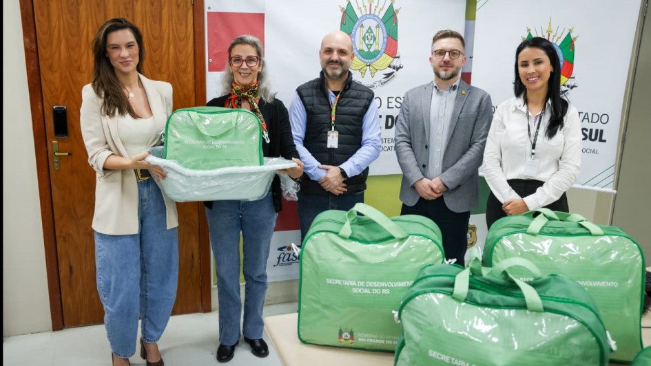 Foto mostra secret&aacute;rios e coordenadoras com kits. Os kits s&atilde;o bolsas verdes. Duas mulheres seguram um dos kits que est&aacute; dentro de uma banheira branca de beb&ecirc;.
