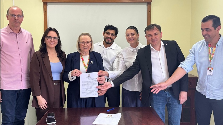 Foto mostra secret&aacute;ria e representantes do hospital exibindo o documento assinado.
