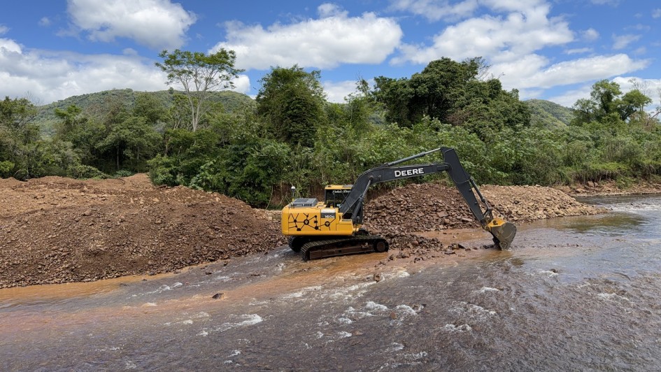 imagem mostra uma m&aacute;quina escavadeira retirando sedimentos de um rio raso.